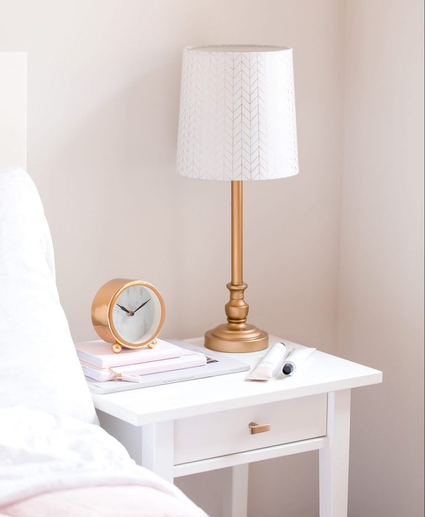 Bedside lamp on night table in bedroom with clock and books on top