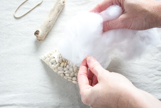 adding white stuffing to a plastic bag filled with dried beans