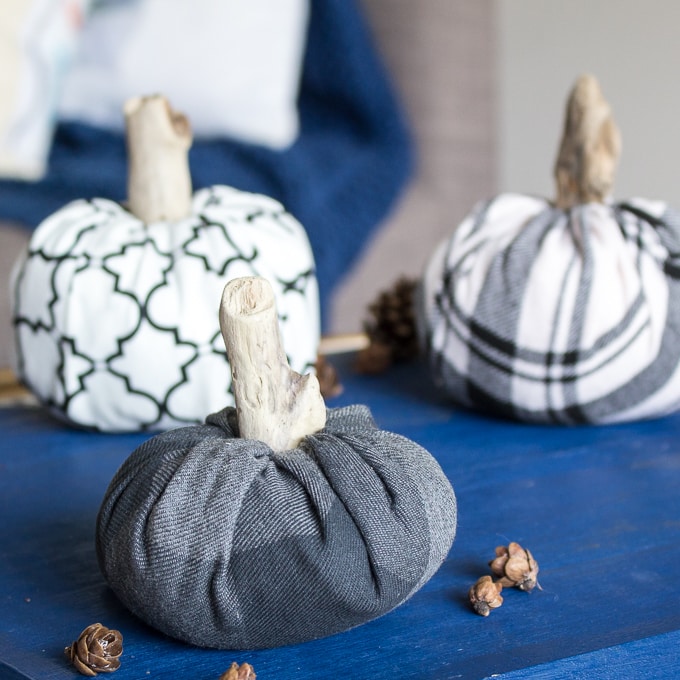 fabric pumpkins with driftwood stems on blue background with pinecones