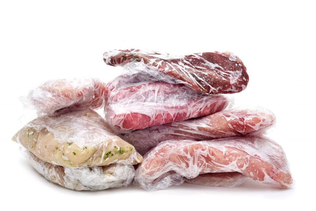 frozen raw meat, such as pork, chicken or beef, wrapped in plastic on a white background