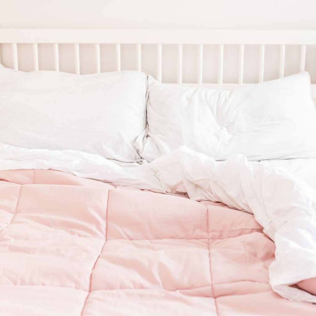 comfy bed with white sheets and pink duvet cover against white wood headboard