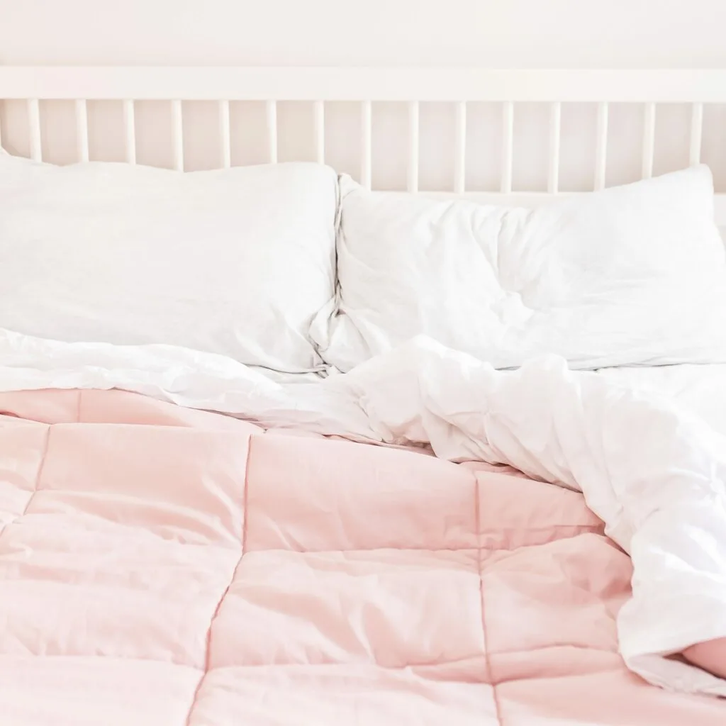 comfy bed with white sheets and pink duvet cover against white wood headboard