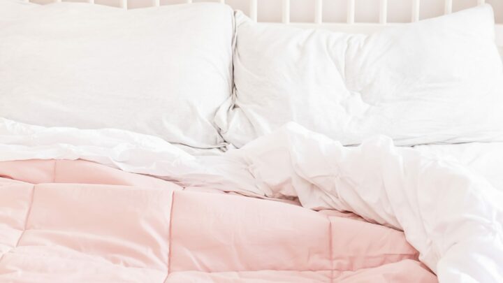 comfy bed with white sheets and pink duvet cover against white wood headboard