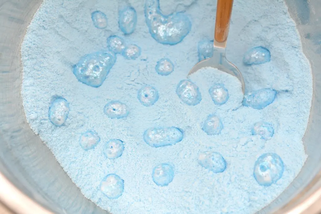 blue powder in a bowl with liquid droplets on top of toilet bowl cleaner tablet mixture