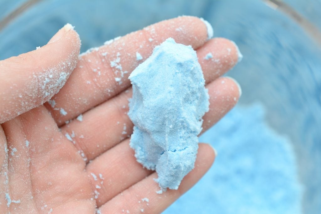 woman's hand with blue powder clump in fingers for toilet bowl fizzies