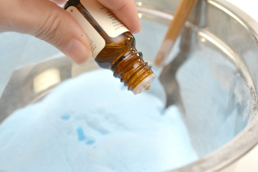 woman's hand adding essential oils from a brown glass bottle into blue powder for toilet bowl cleaner tablets