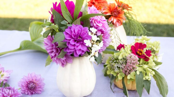 purple and orange flowers with greenery in white pumpkin flower vase on table