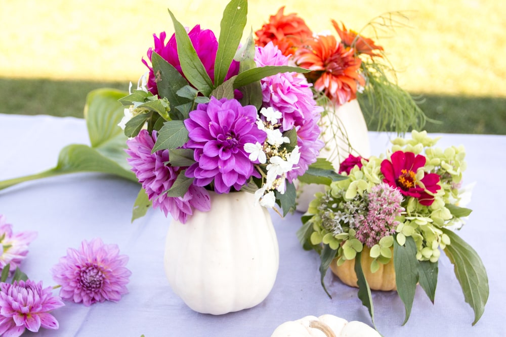 purple and orange flowers with greenery in white pumpkin flower vase on table