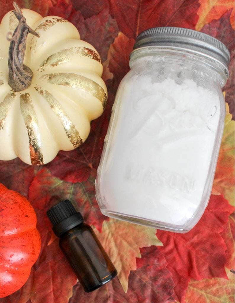glass jar with baking soda inside on fall leaves and orange pumpkins with essential oil bottle 