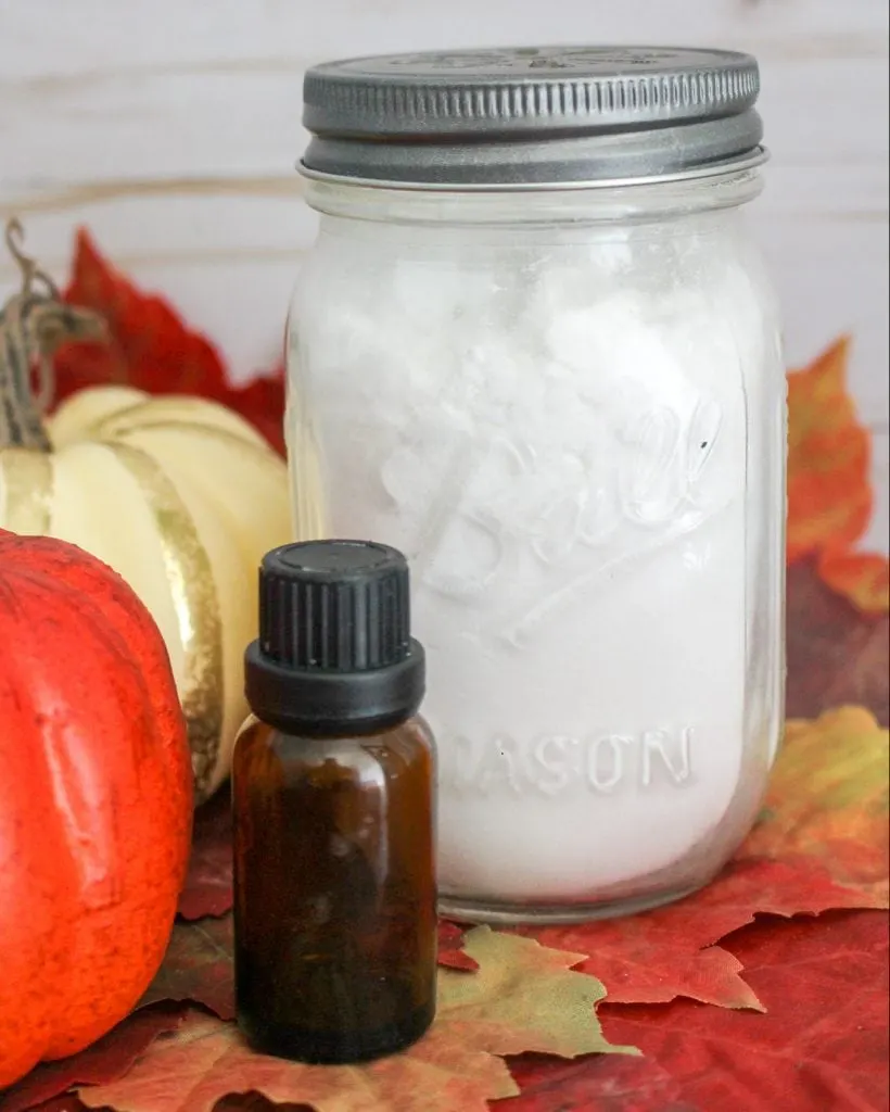 Glass jar with white baking soda against pumpkins, white wood background, fall leaves and essential oil bottle