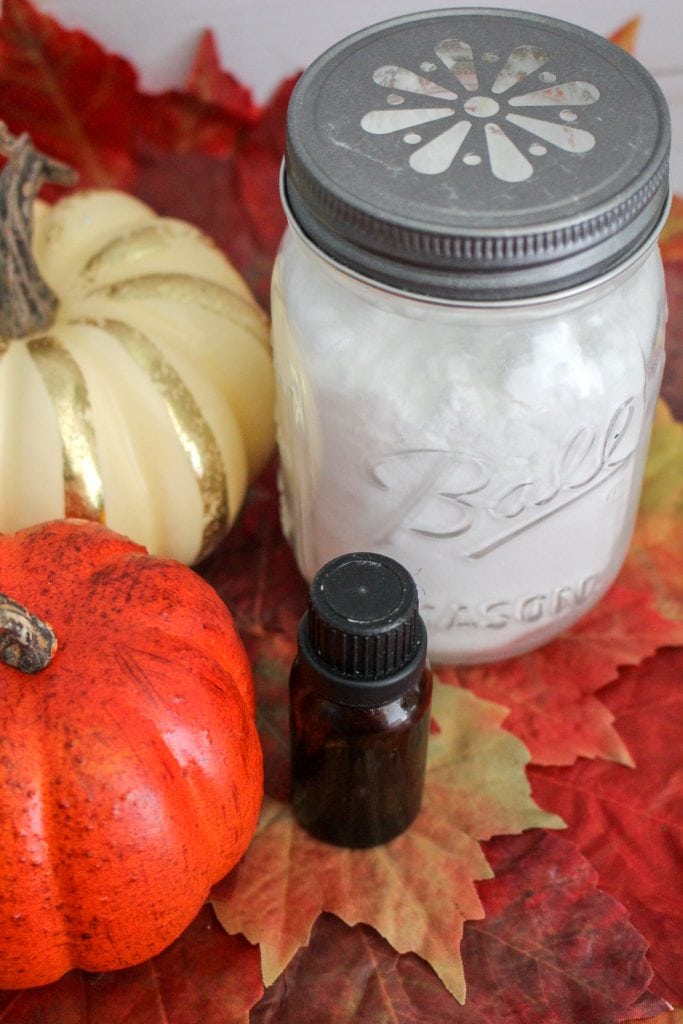 Glass jar with white baking soda against pumpkins, white wood background, fall leaves and essential oil bottle