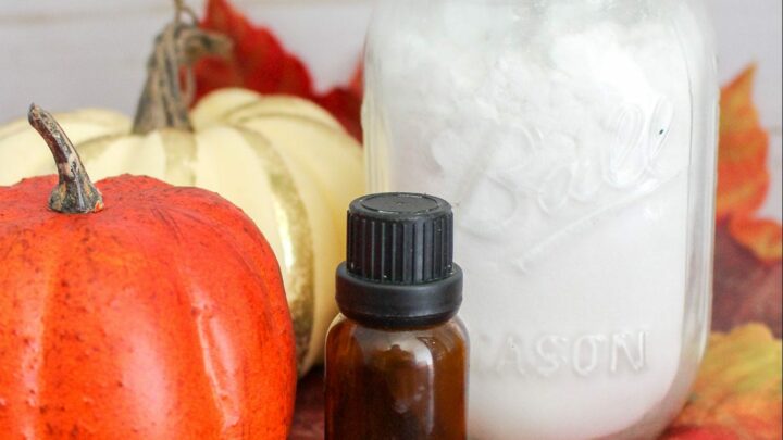 Glass jar with white baking soda against pumpkins, white wood background, fall leaves and essential oil bottle