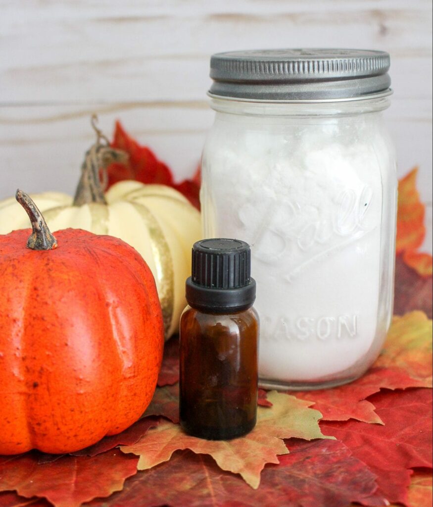 Glass jar with white baking soda against pumpkins, white wood background, fall leaves and essential oil bottle