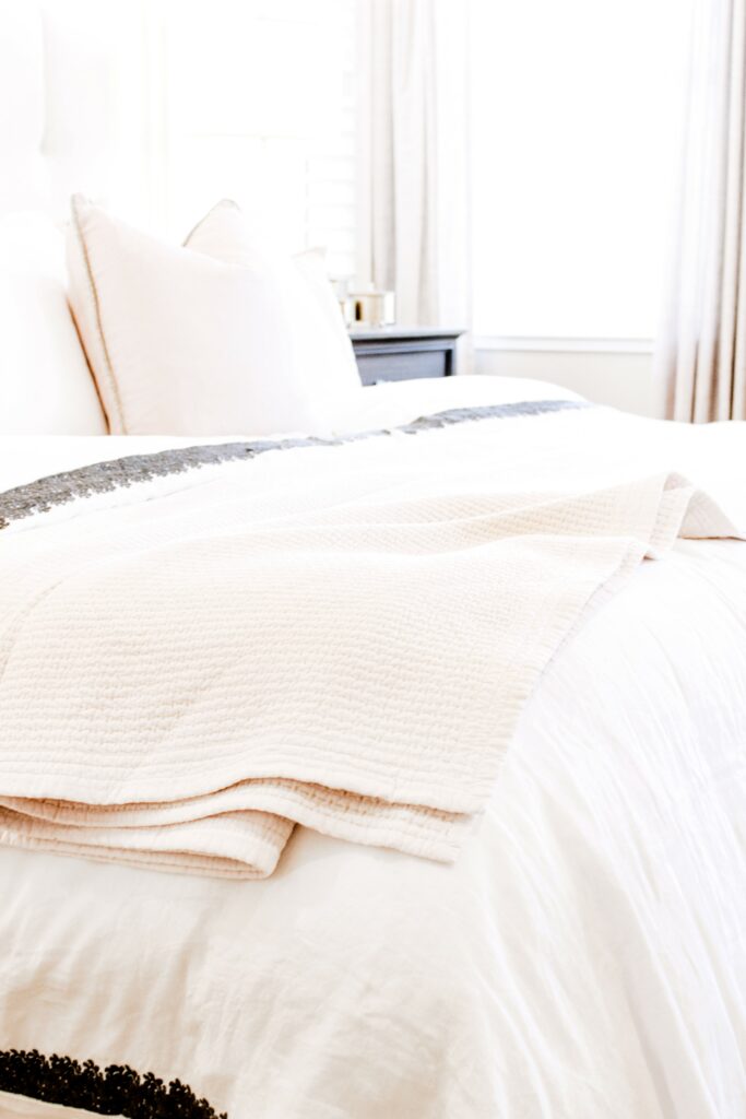 bed with pale pink blush sheets and bedding near window with sunlight