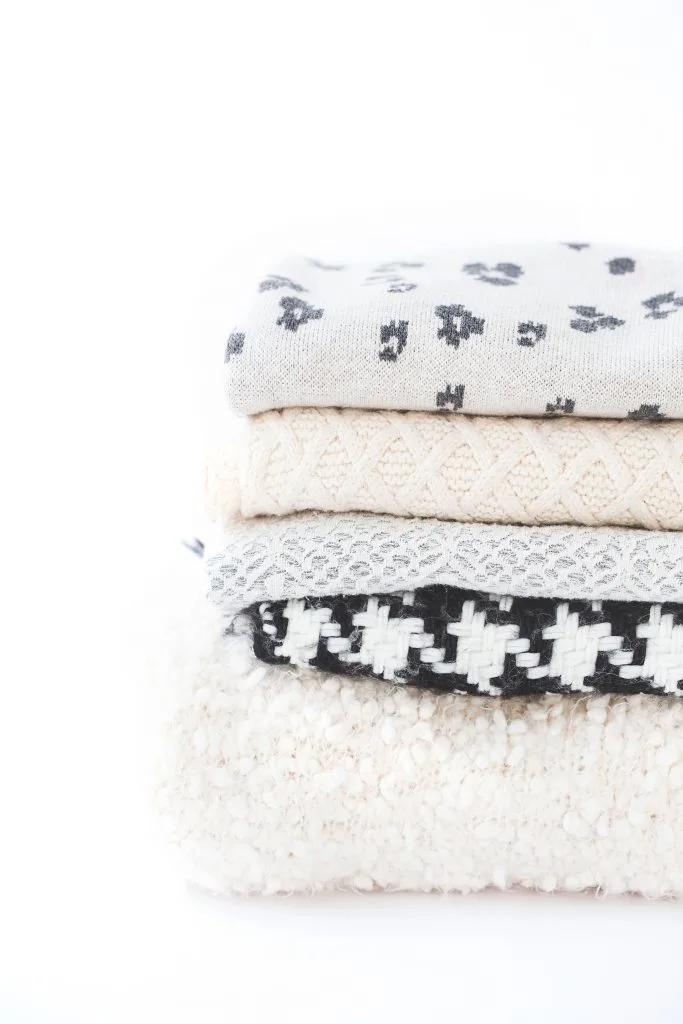 cozy grey, white, and black blankets stacked up against a white background