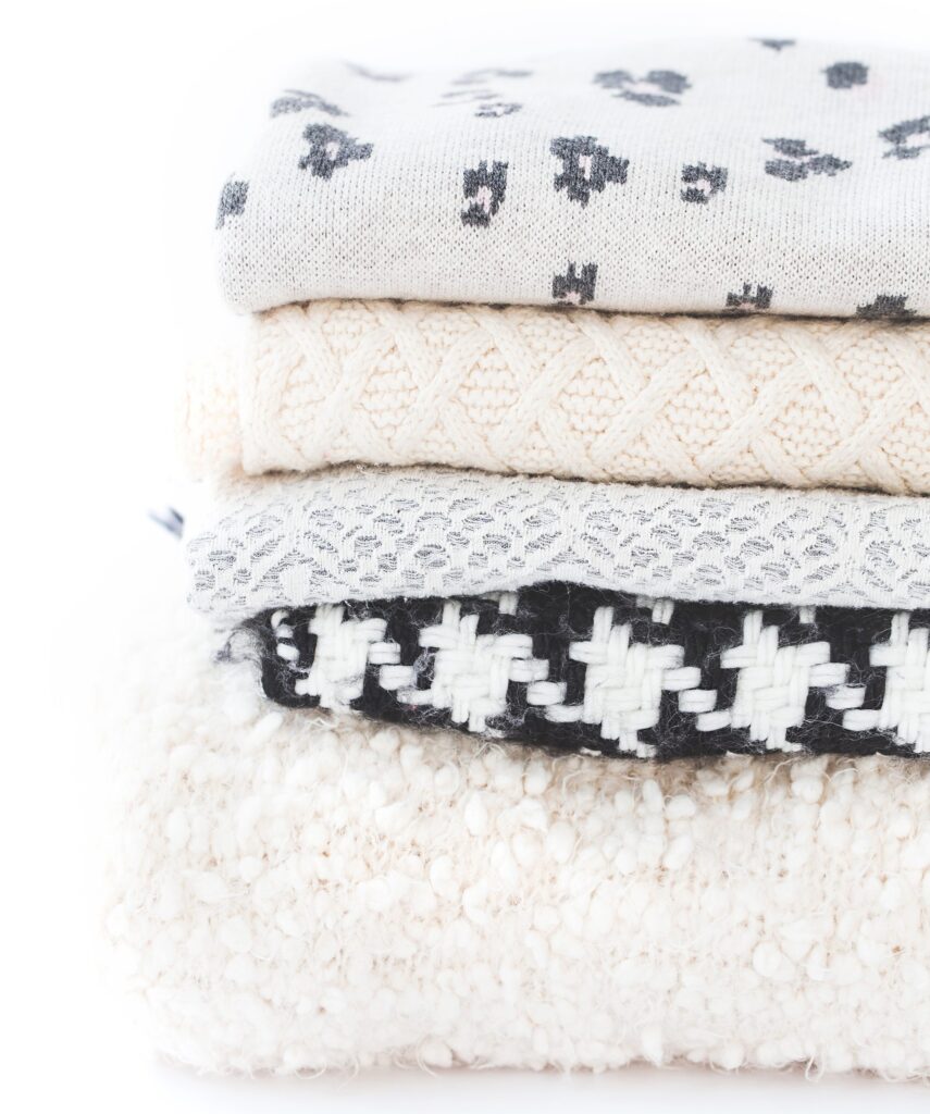 cozy grey, white, and black blankets stacked up against a white background