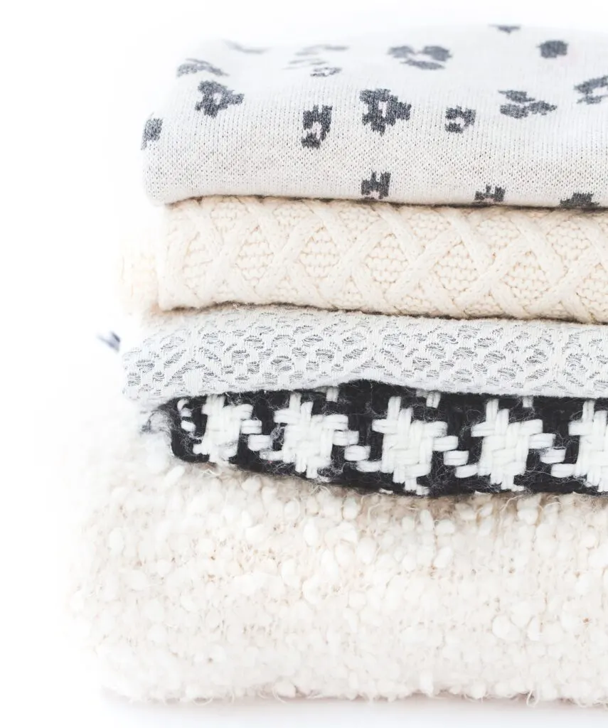 cozy grey, white, and black blankets stacked up against a white background