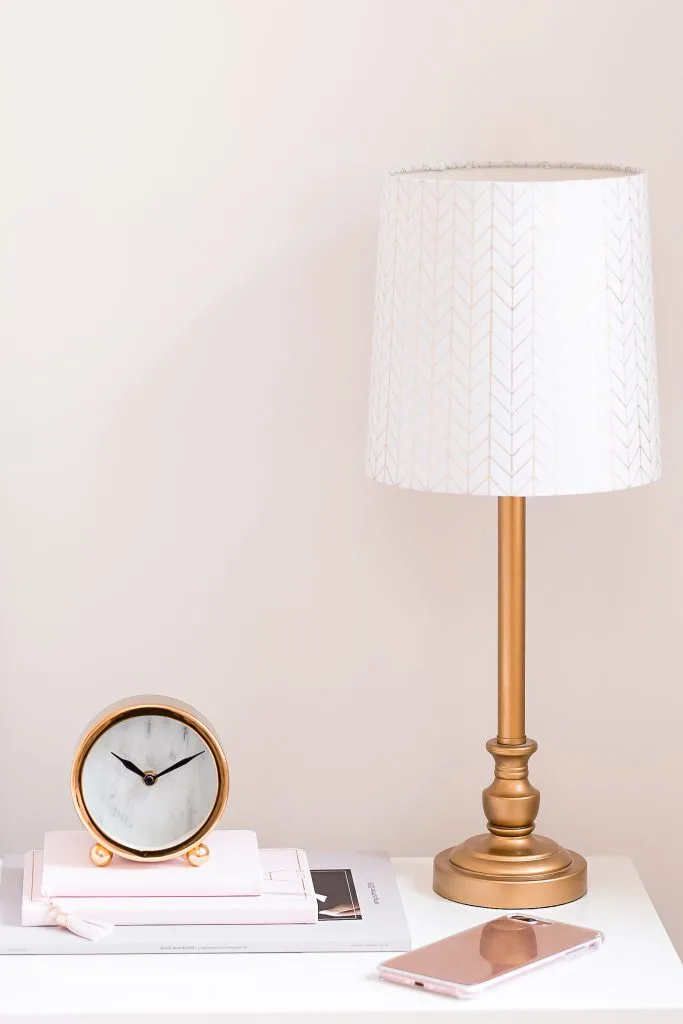 nightstand with gold lamp and battery operated clock on books against pink wall