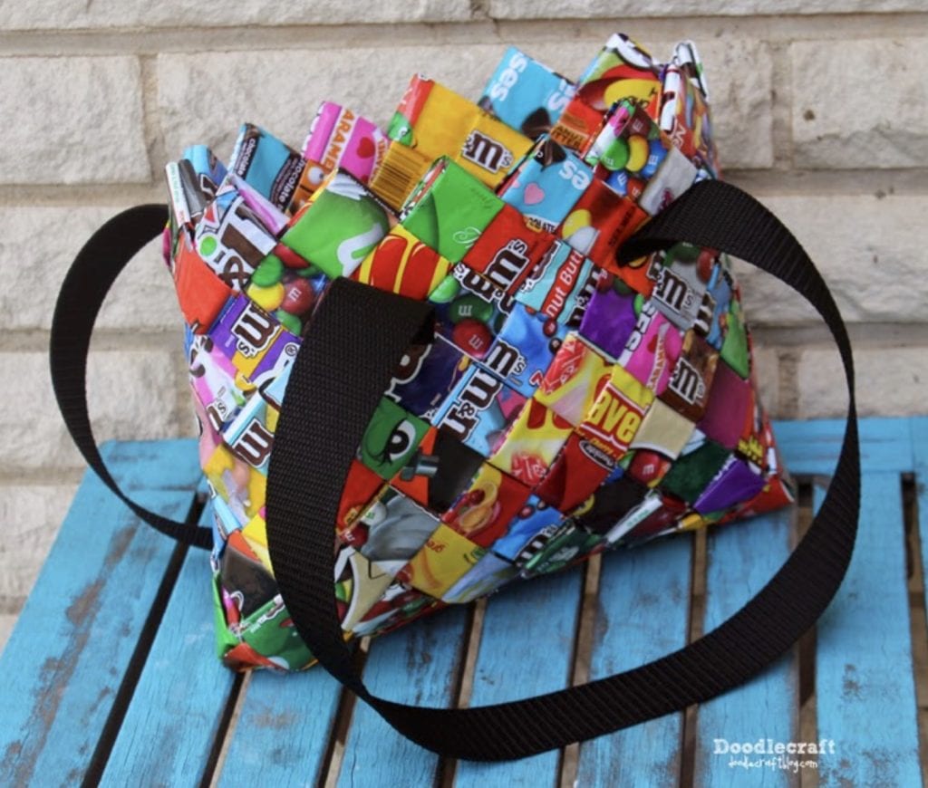 purse made out of candy wrappers with black handles on blue table