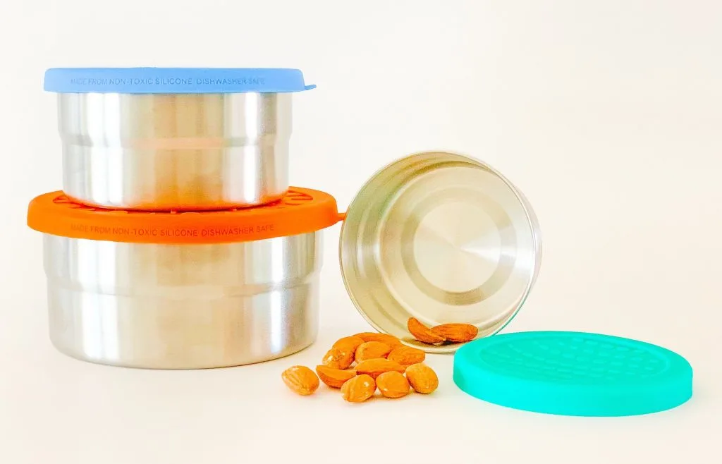three stainless steel storage containers with blue, orange and teal colored silicone lids and almonds on white background