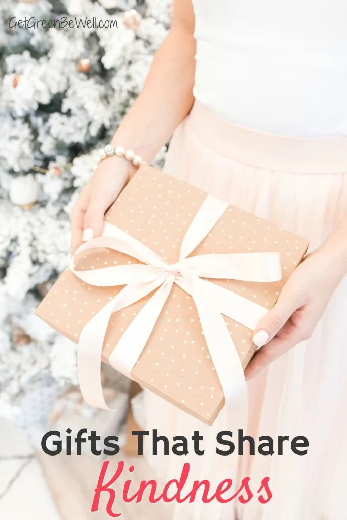 woman in pink skirt holding brown wrapped gift with pink bow against Christmas tree covered in white snow