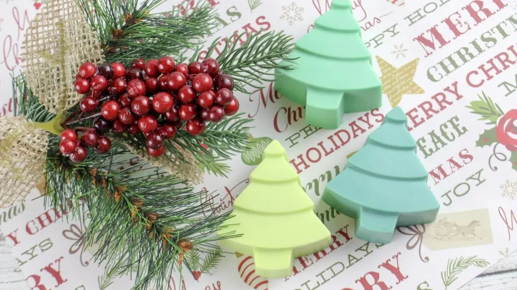 three christmas tree soaps in different shades of green next to pine needles and holly berries