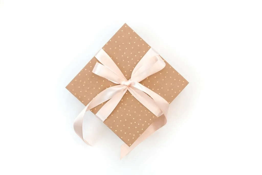 gift wrapped in brown and gold polka dot wrapping paper with pink bow against white background