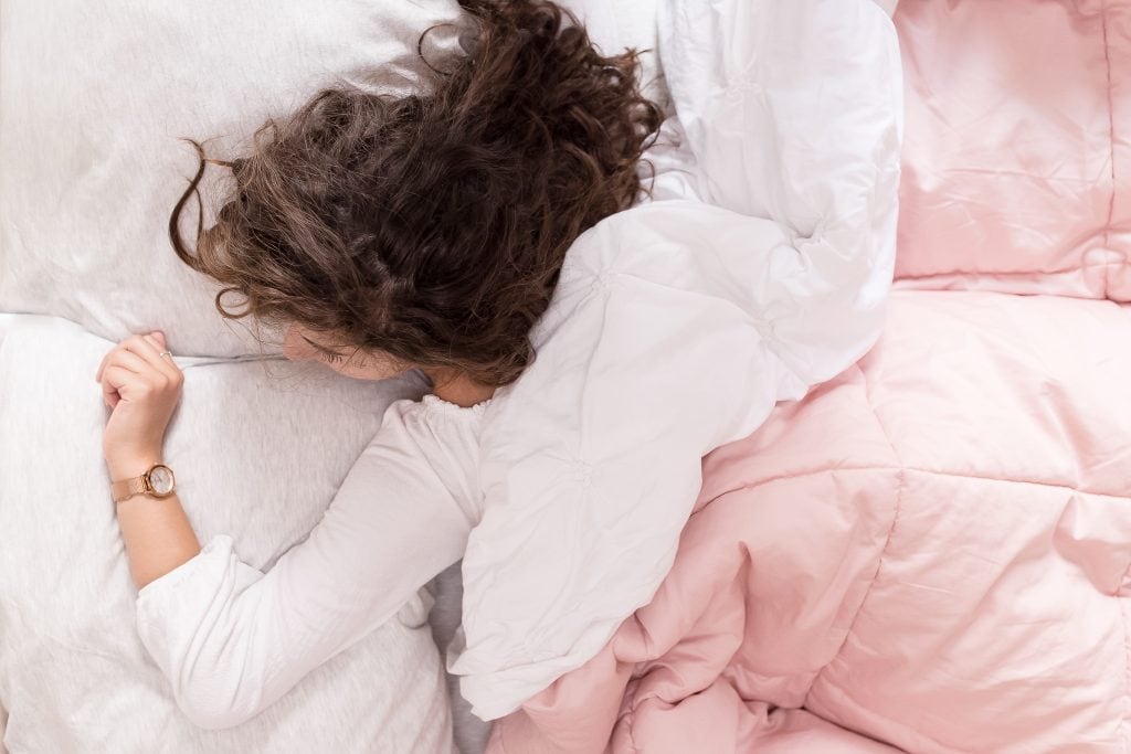 woman looking at watch while lying under heavy pink comforter and white blanket