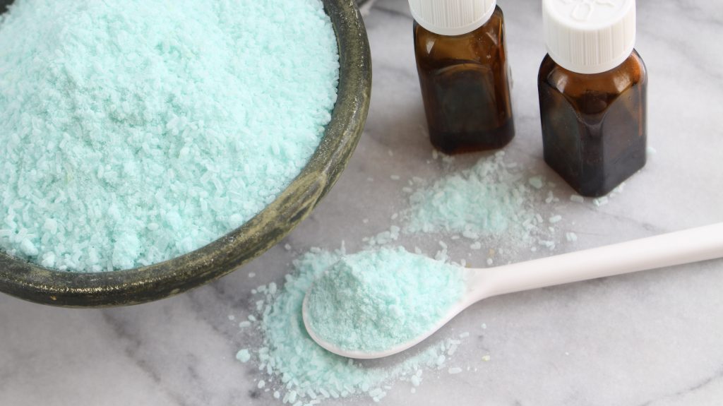 Sinus Congestion relief bath salts in wooden bowl with spoon and brown essential oil bottles on marble background