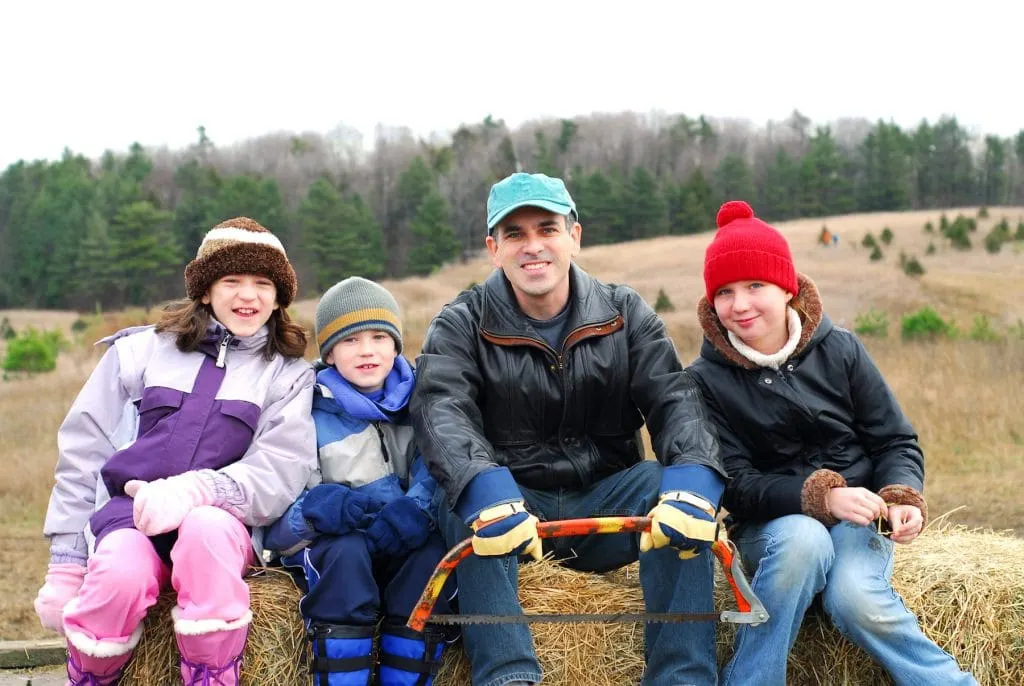 family wearing winter clothes sitting in forest before cutting a Christmas tree