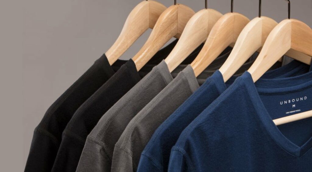 black grey and blue wool shirts hanging on wooden hangers against gray background