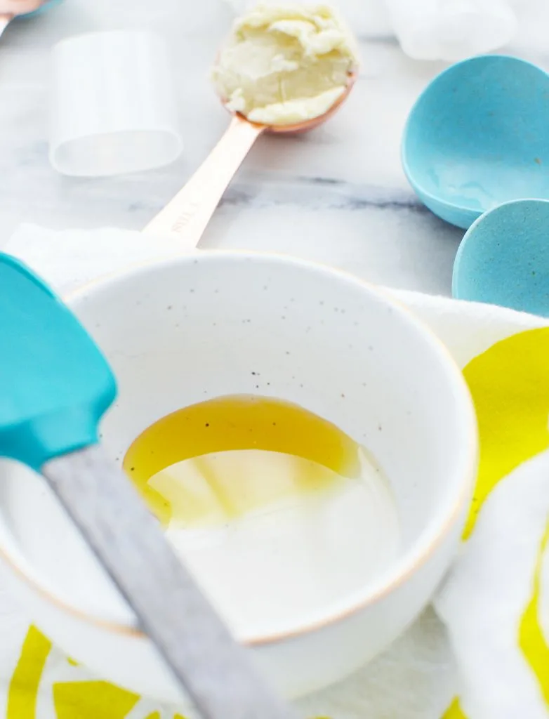 liquid oil in white ceramic bowl with blue spatula against white marble table