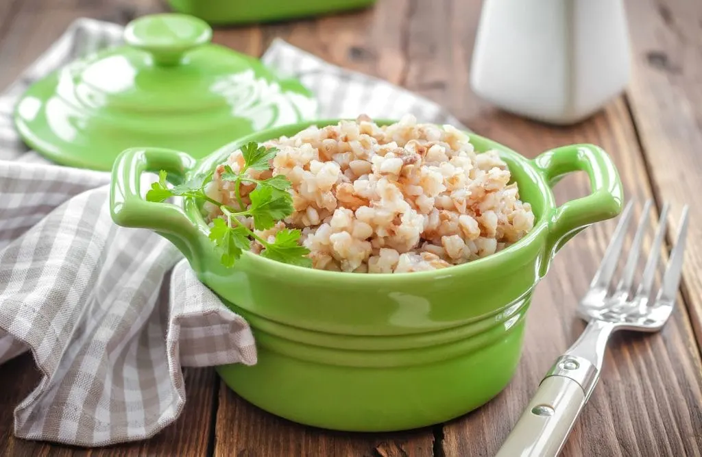 green ceramic crock with buckwheat hot cereal on wooden table with grey towel