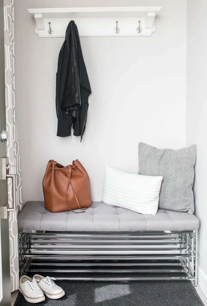 wire bench in entry way with grey cushions brown leather purse and coat hanging on hooks