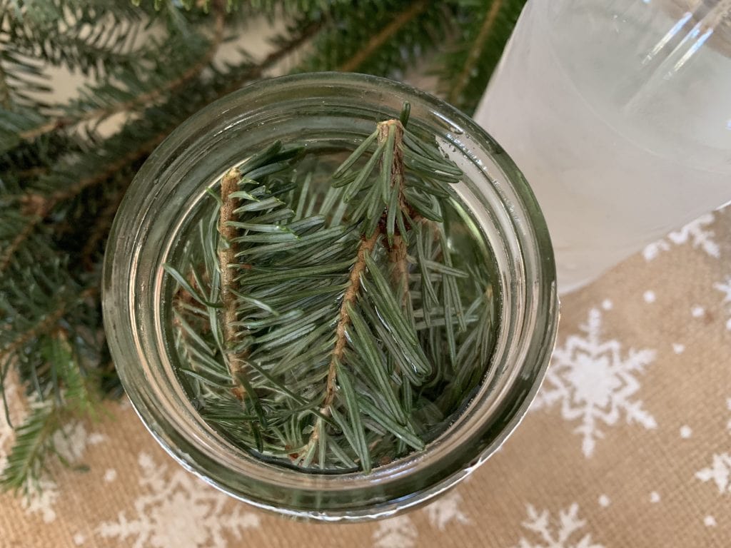 pine branches in open glass mason jar against burlap tablecloth with white snowflakes to make scented vinegar