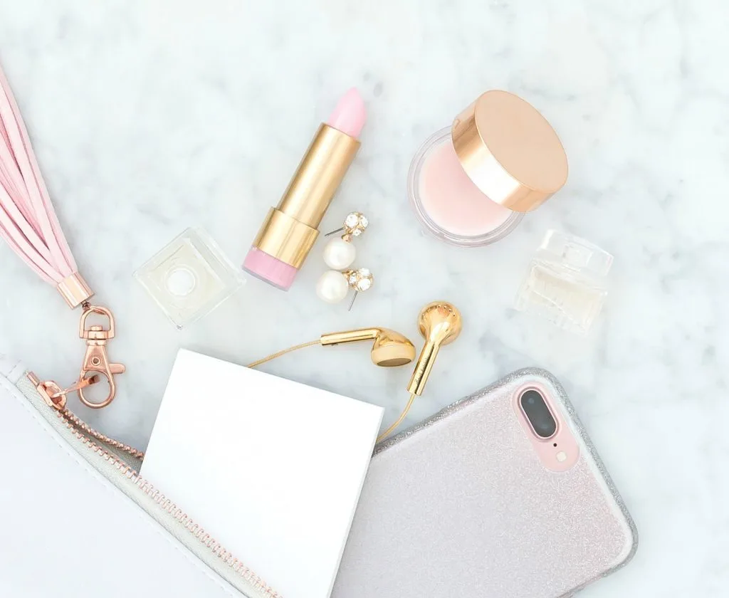 emptied purse with lipstick makeup phone earrings and ear buds with pink leather tassel against white marble background