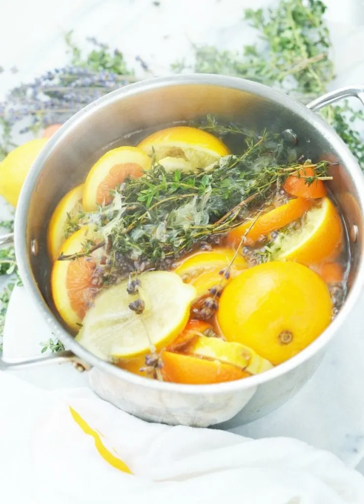 orange lemon lavender thyme herb in boiling water in stainless steel simmer pot on white marble stove top potpourri