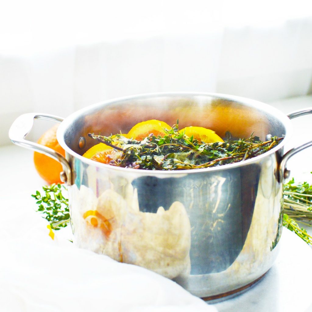 sliced oranges and lemons in stainless steel simmer pot against white marble for natural air freshener