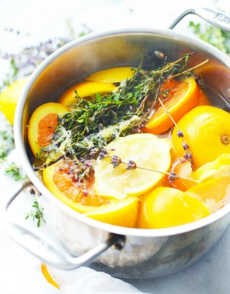 orange lemon lavender thyme herb in boiling water in stainless steel simmer pot on white marble stove top potpourri