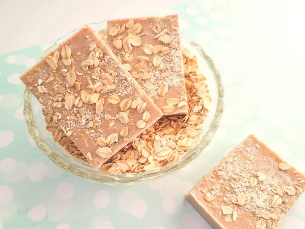 exfoliating Cinnamon Oatmeal Soap bar in glass bowl of rolled oats on blue background