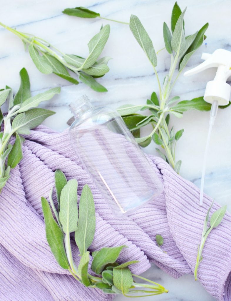 glass spray bottle against purple cleaning cloth fresh sage leaves