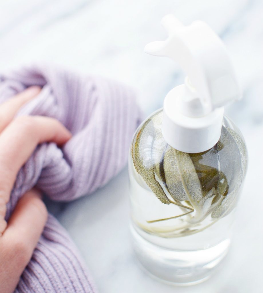 woman holding purple cloth next to glass bottle of DIY sage spray 