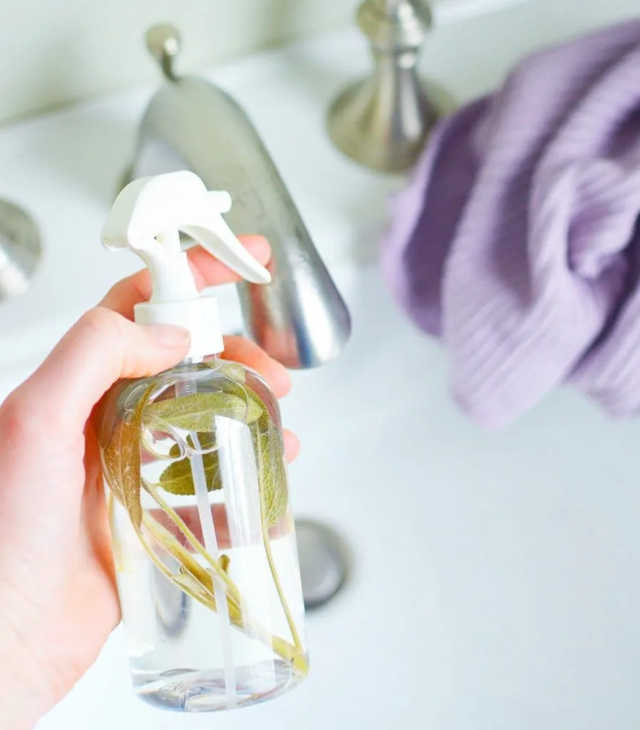 woman holding glass spray bottle filled with sage leaves for DIY spray