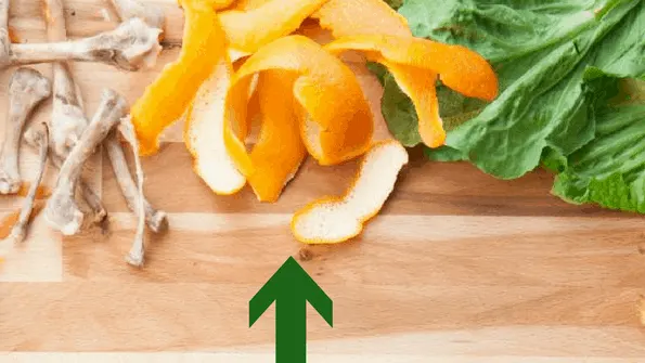 citrus peels and green leaves food waste on wood board