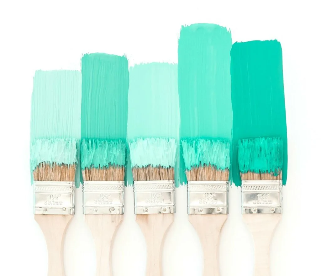 five paint brushes coated in green paint against white background