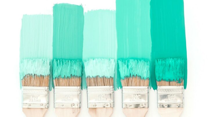 five paint brushes coated in green paint against white background