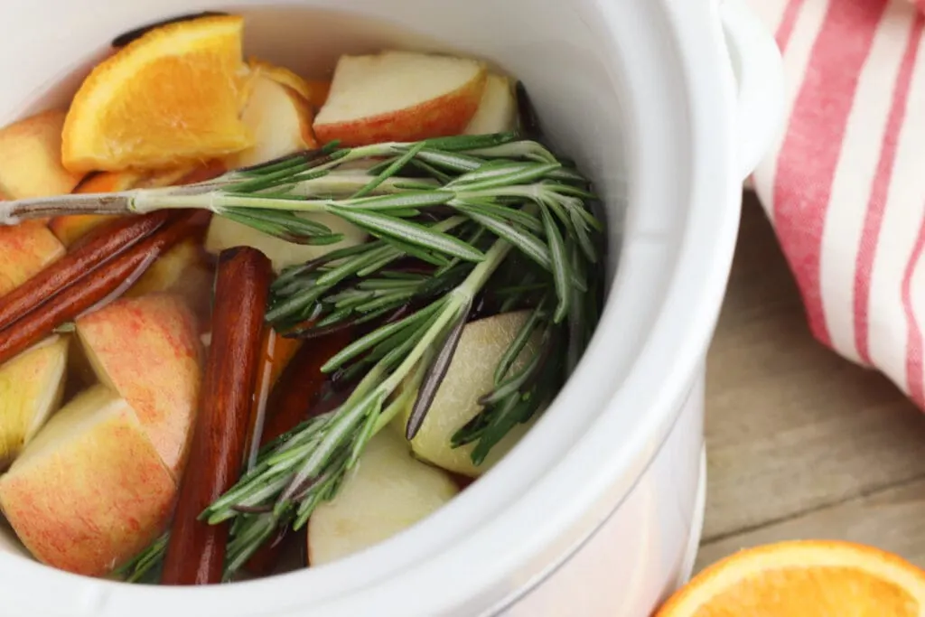 oranges apples cinnamon sticks and rosemary in a white crock pot potpourri 