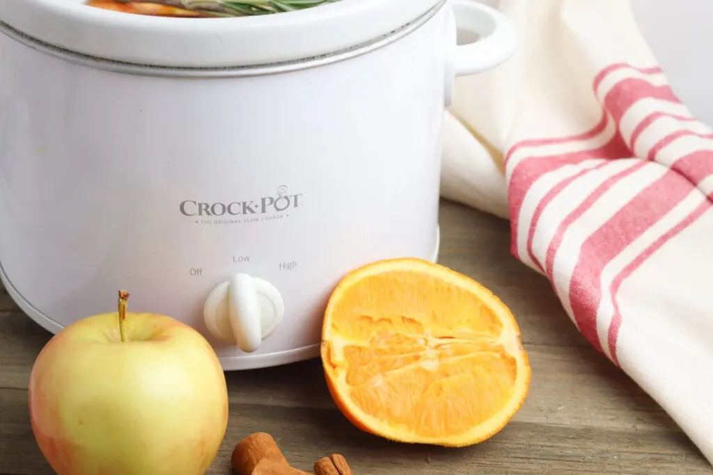 white crock pot with apples and oranges on wooden table