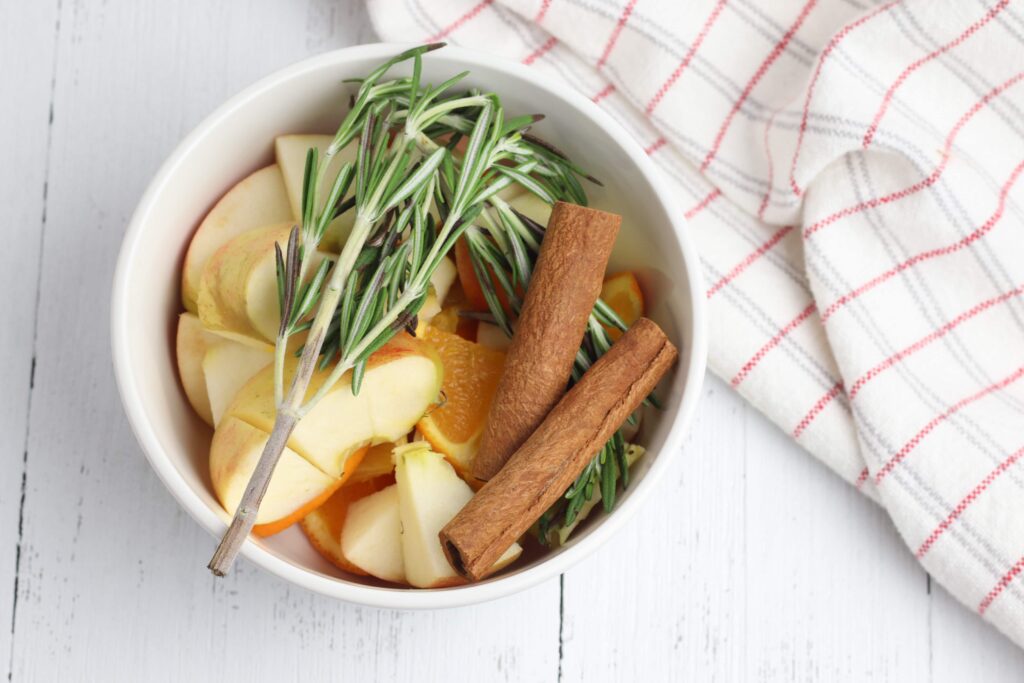 apples cinnamon sticks and rosemary in a white crock pot