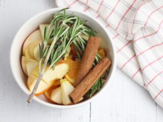 apples cinnamon sticks and rosemary in a white crock pot